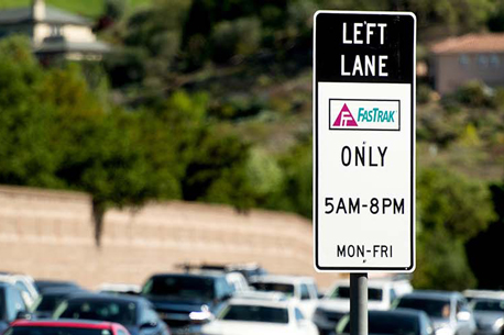 Long line of rush hour traffic with an express lanes roadsign, showing express lane times and FasTrak tag requirement